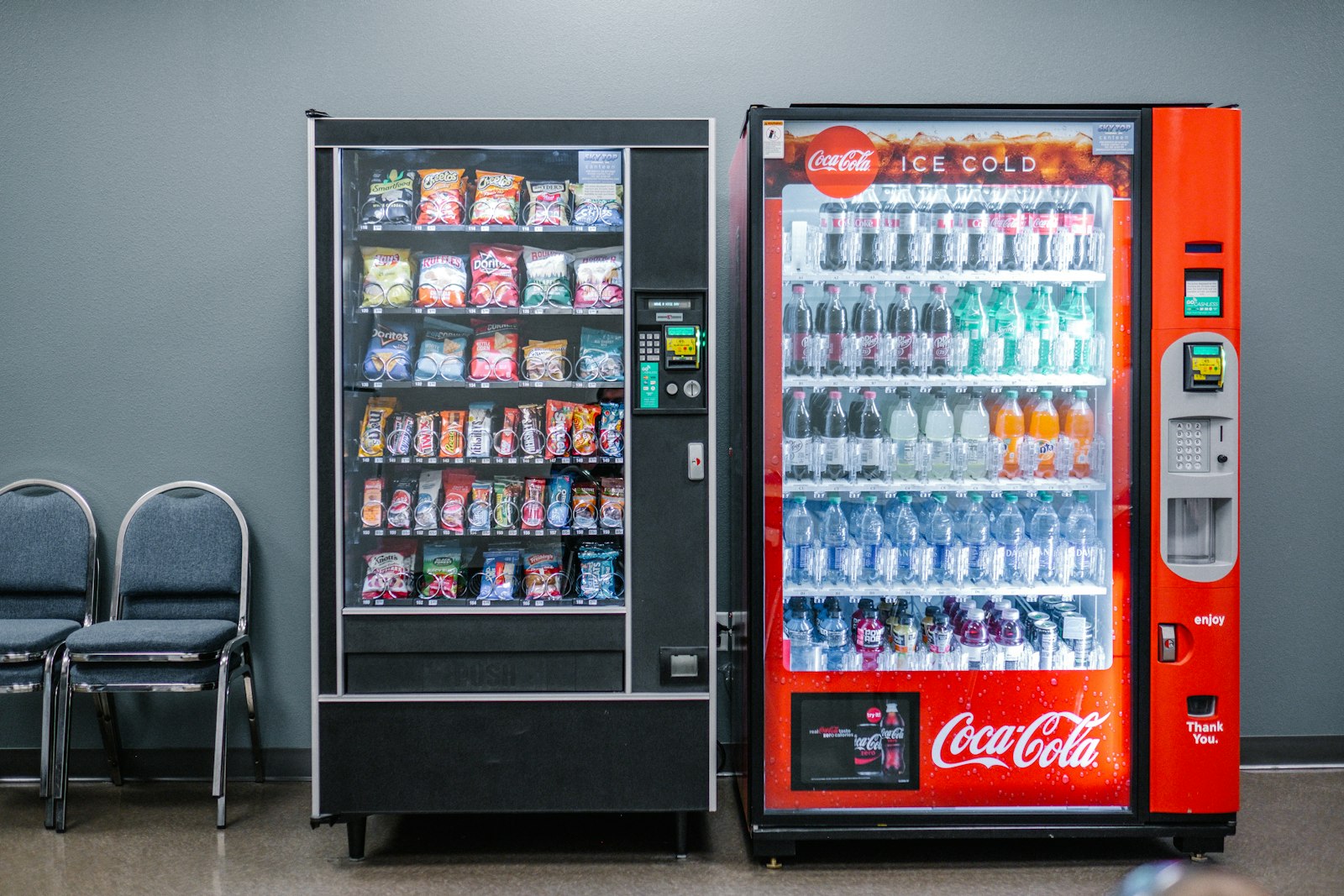 A black snack vending machine beside a red bottled-drink machine, shown as an example of traditional vending.